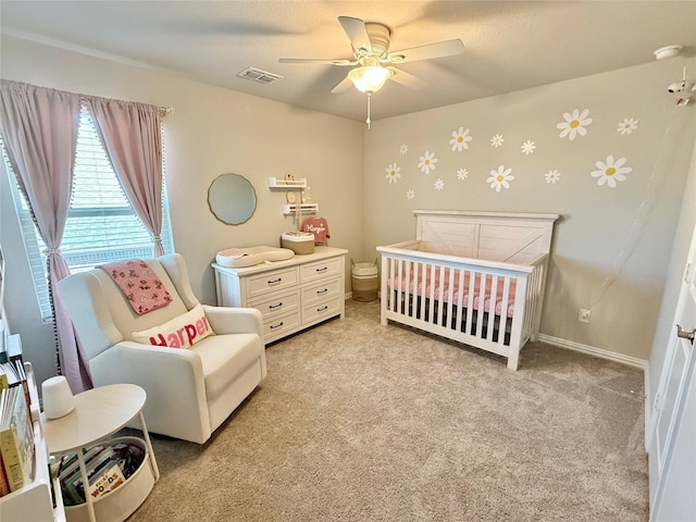 bedroom with visible vents, a ceiling fan, light carpet, a nursery area, and baseboards