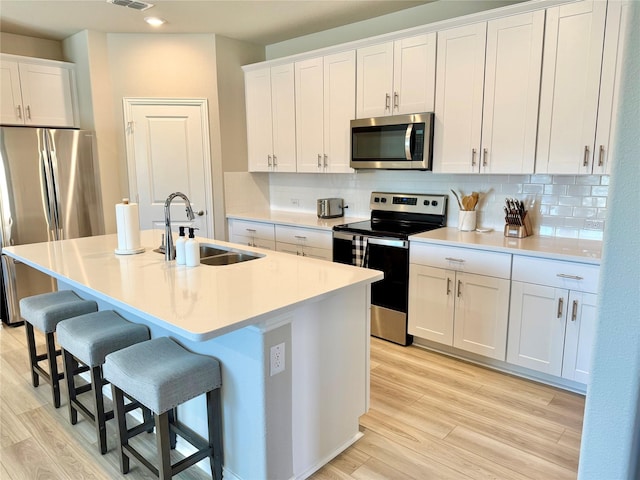 kitchen featuring appliances with stainless steel finishes, light countertops, white cabinetry, and a center island with sink