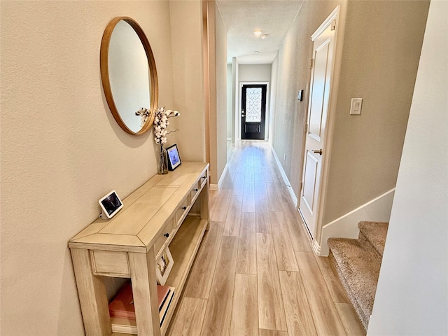 corridor with baseboards, stairway, and light wood-style floors