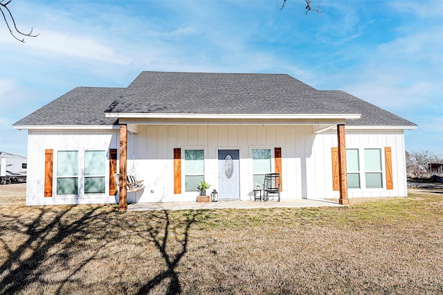 rear view of property featuring board and batten siding, a patio, a shingled roof, and a lawn