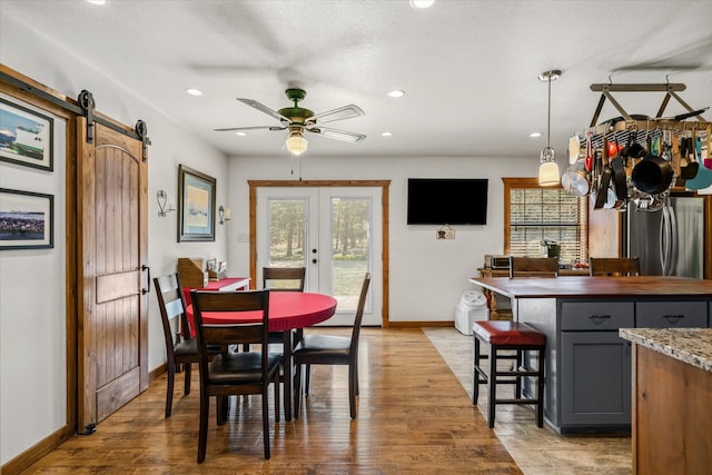 dining area featuring a barn door, baseboards, light wood-style flooring, french doors, and recessed lighting