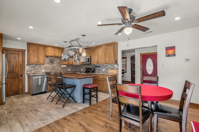 kitchen featuring a center island, decorative light fixtures, stainless steel appliances, visible vents, and brown cabinetry