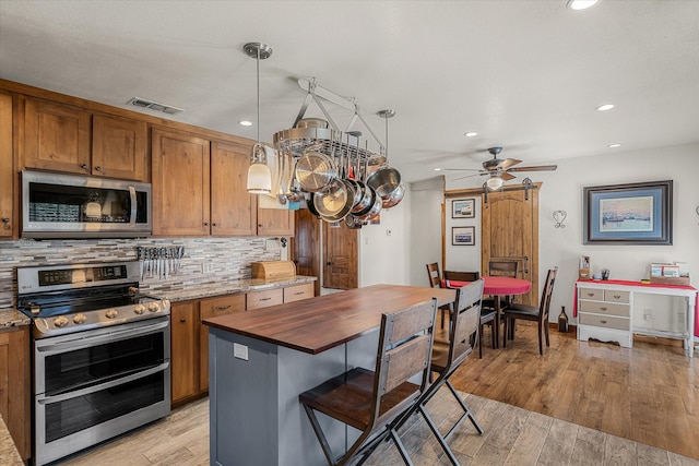 kitchen featuring visible vents, decorative backsplash, appliances with stainless steel finishes, light wood-type flooring, and pendant lighting