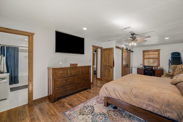 bedroom featuring recessed lighting, visible vents, a barn door, wood finished floors, and baseboards