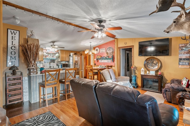 living room featuring vaulted ceiling, a textured ceiling, a glass covered fireplace, and light wood-style floors