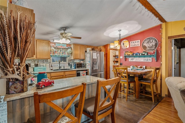 kitchen with light wood finished floors, brown cabinets, hanging light fixtures, stainless steel appliances, and a sink