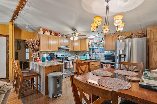 kitchen featuring decorative light fixtures, appliances with stainless steel finishes, a sink, light stone countertops, and under cabinet range hood