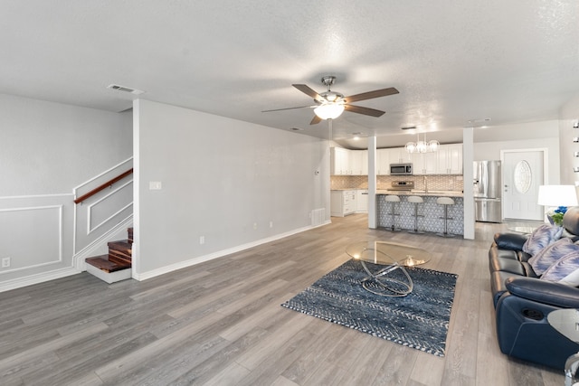 living room featuring ceiling fan with notable chandelier, visible vents, a textured ceiling, wood finished floors, and stairs