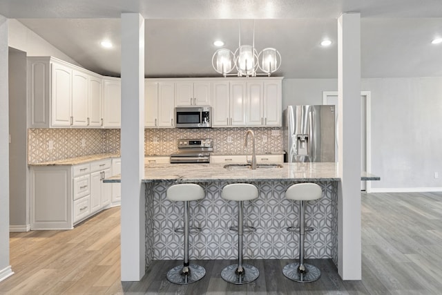 kitchen featuring appliances with stainless steel finishes, a sink, white cabinetry, and light stone countertops