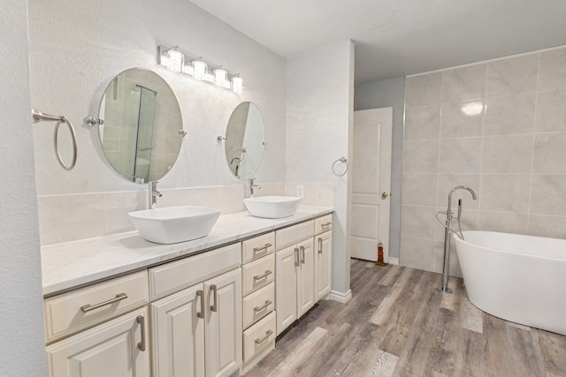 bathroom featuring double vanity, a sink, a freestanding bath, and wood finished floors