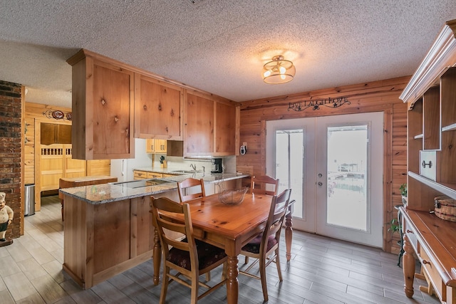 dining area featuring light wood-type flooring, wooden walls, a textured ceiling, and french doors