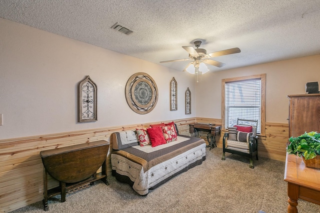 carpeted living room featuring visible vents, a ceiling fan, a wainscoted wall, a textured ceiling, and wood walls