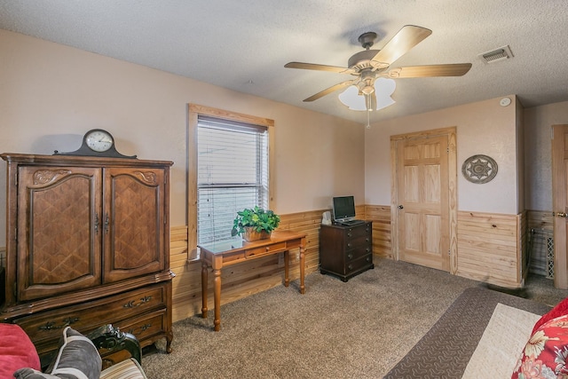 office space featuring a textured ceiling, wooden walls, a wainscoted wall, carpet floors, and visible vents