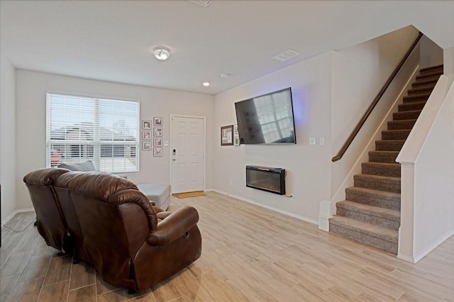 living area with light wood-style flooring, stairs, baseboards, and a glass covered fireplace