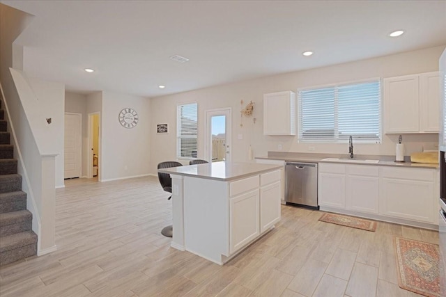 kitchen featuring light countertops, white cabinets, a kitchen island, a sink, and dishwasher