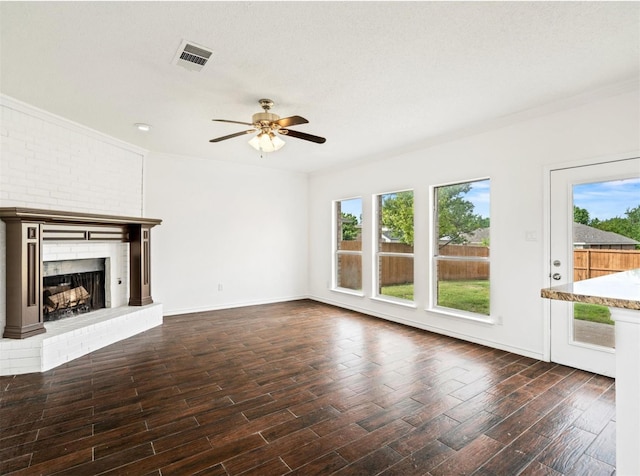 unfurnished living room featuring crown molding, visible vents, dark wood-type flooring, a ceiling fan, and a brick fireplace