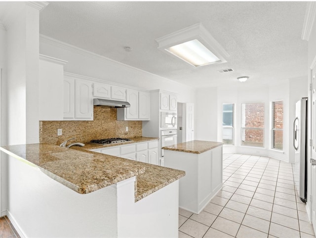 kitchen with a center island, appliances with stainless steel finishes, white cabinetry, a peninsula, and under cabinet range hood