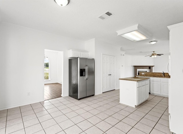 kitchen featuring stainless steel refrigerator with ice dispenser, light tile patterned floors, dark countertops, visible vents, and white cabinetry