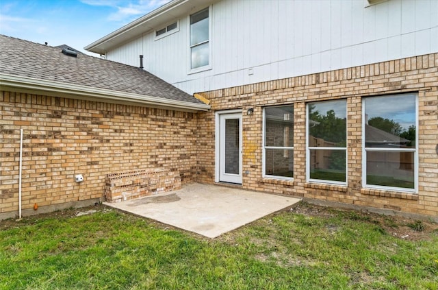 entrance to property with brick siding, a patio, a lawn, and roof with shingles