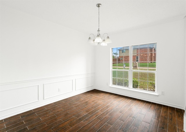 unfurnished room with dark wood-type flooring, a chandelier, a wainscoted wall, and a decorative wall