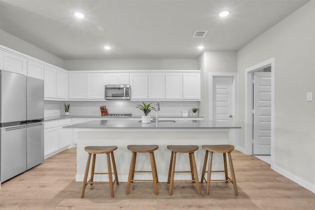 kitchen with stainless steel appliances, visible vents, white cabinetry, a sink, and light wood-type flooring