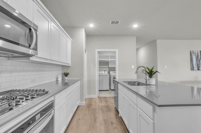 kitchen featuring visible vents, an island with sink, independent washer and dryer, stainless steel appliances, and a sink