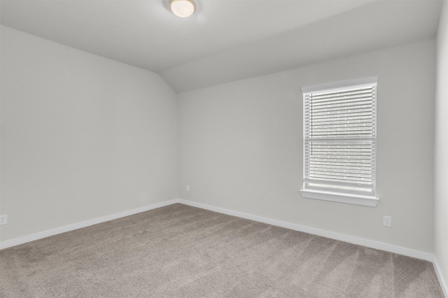 carpeted empty room featuring baseboards and vaulted ceiling