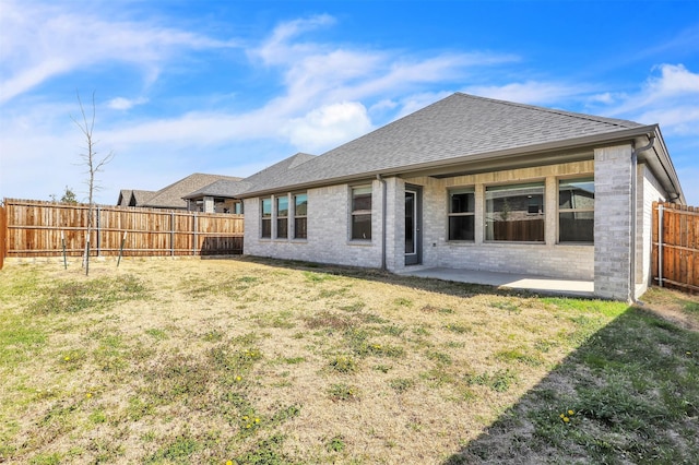 rear view of house featuring a patio, a yard, a shingled roof, and a fenced backyard