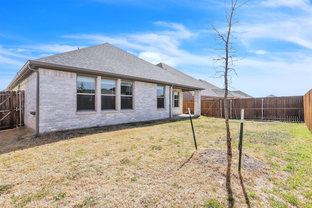 back of property with a shingled roof, brick siding, a lawn, and a fenced backyard