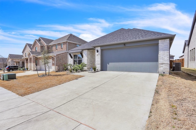 view of front of property featuring driveway, a shingled roof, stone siding, an attached garage, and central AC