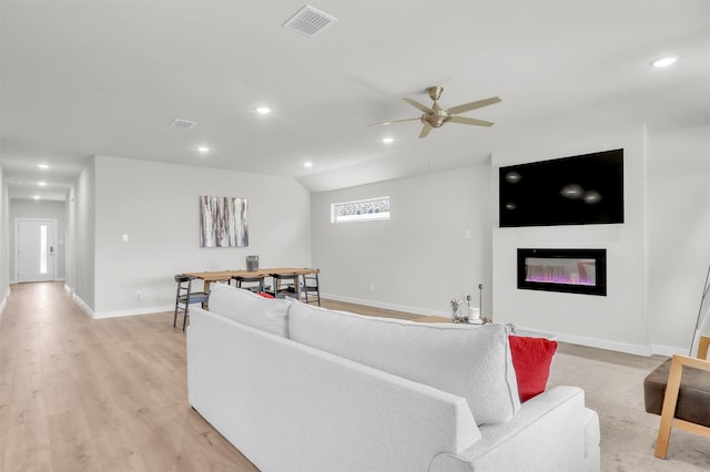 living area with recessed lighting, visible vents, light wood-style flooring, a glass covered fireplace, and baseboards