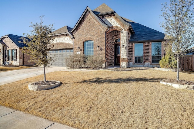 french country inspired facade with driveway, a garage, brick siding, stone siding, and a front yard