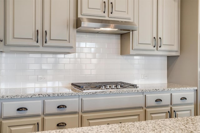 kitchen featuring stainless steel gas cooktop, decorative backsplash, light stone countertops, and under cabinet range hood