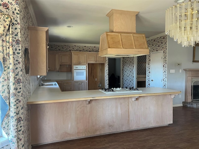 kitchen featuring a peninsula, white appliances, light countertops, custom exhaust hood, and crown molding