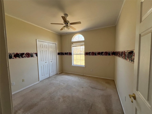 empty room with ornamental molding, light colored carpet, baseboards, and a ceiling fan