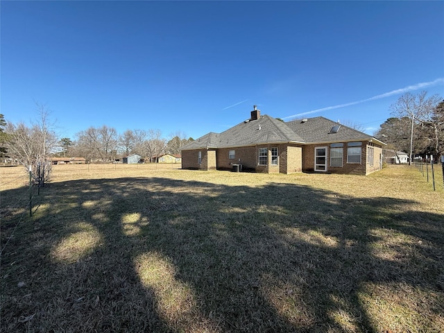 rear view of property featuring a yard, brick siding, a chimney, and fence