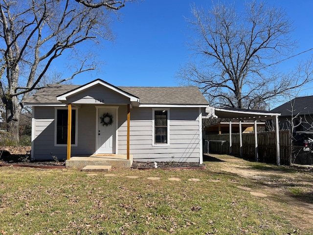 bungalow with a carport, roof with shingles, dirt driveway, and a front lawn