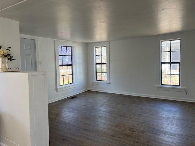 unfurnished room with dark wood-type flooring, visible vents, and baseboards