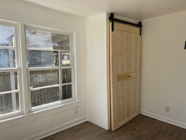 empty room featuring a barn door, baseboards, and dark wood-style flooring