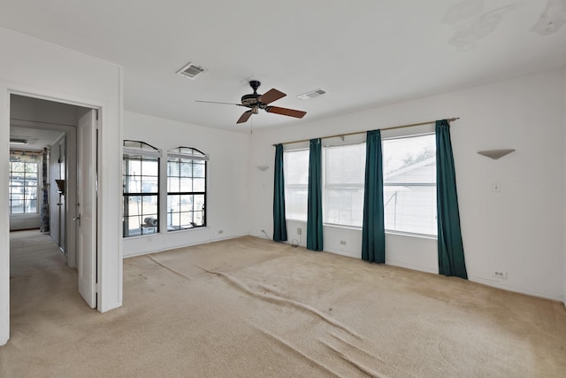 empty room featuring a ceiling fan, visible vents, and light colored carpet