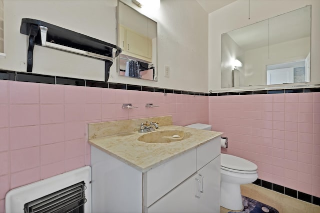 half bath featuring tile walls, toilet, wainscoting, vanity, and tile patterned floors