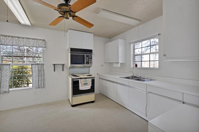 kitchen featuring electric stove, light countertops, white cabinetry, a sink, and black microwave