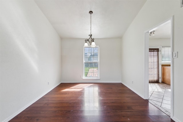 empty room with a chandelier, wood finished floors, and baseboards