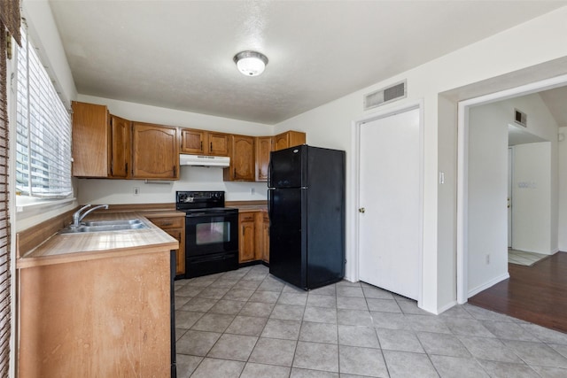 kitchen featuring visible vents, brown cabinetry, under cabinet range hood, black appliances, and a sink