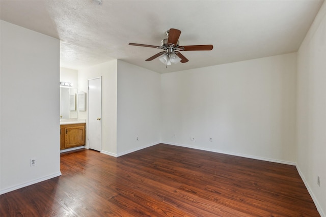 unfurnished bedroom featuring ceiling fan, baseboards, dark wood finished floors, and ensuite bathroom