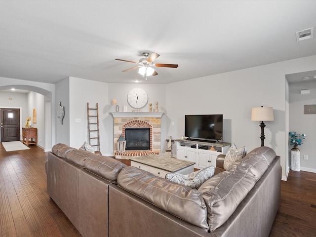 living area with arched walkways, a ceiling fan, visible vents, baseboards, and dark wood finished floors