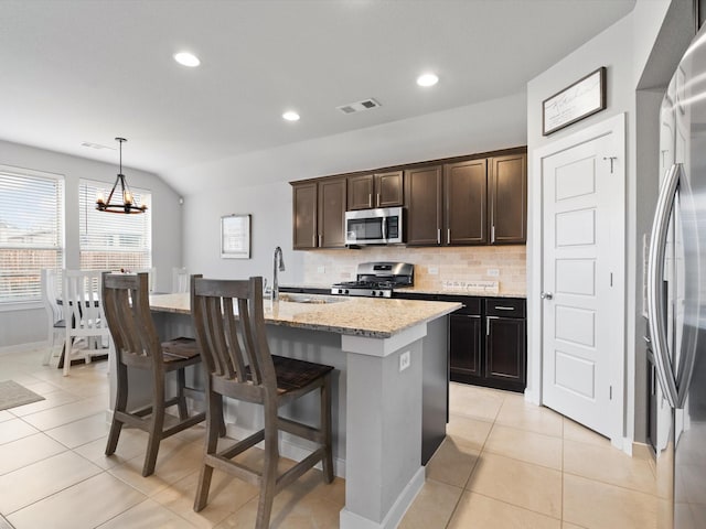 kitchen featuring decorative light fixtures, visible vents, appliances with stainless steel finishes, light stone countertops, and a center island with sink