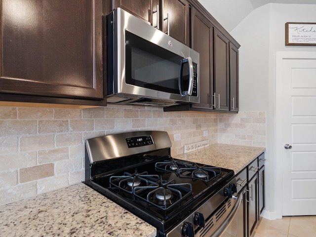 kitchen featuring light tile patterned floors, backsplash, appliances with stainless steel finishes, dark brown cabinetry, and light stone countertops