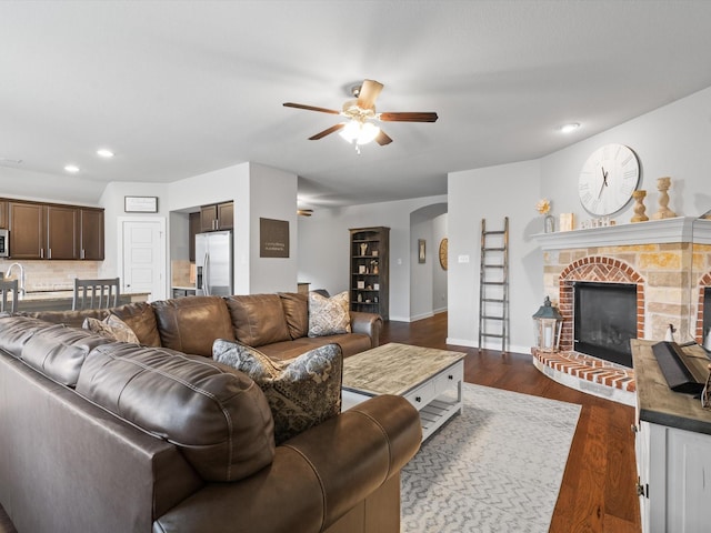 living area with ceiling fan, recessed lighting, baseboards, a brick fireplace, and dark wood-style floors