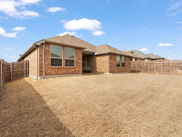 back of property featuring a fenced backyard, brick siding, and roof with shingles